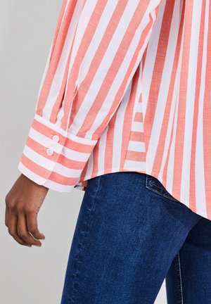 Gaisma, koraļļu un baltas svītras garām piedurknēm krekls ar pogājamiem aprocēm, kombinēts ar tumši zilām džinsa biksēm. Teksturēta auduma un brīva piegriezuma.