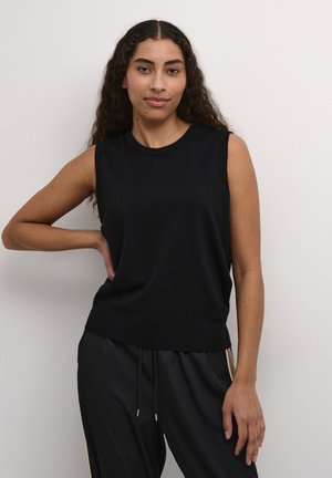 Pulover negru fără mâneci, cu guler rotund, margini din jerseu și o croială lejeră, purtat cu pantaloni negri cu accente laterale.