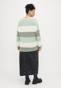 Svijetlozeleni i sivi prugasti pleteni pulover s opuštenim krojem, uparen s crnom traper max suknjom i glomaznim crnim čizmama.