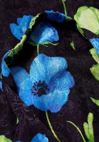 Floral fabric featuring large blue flowers and green leaves on a black patterned background, with a slightly textured surface and gathered edge.