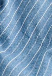 Tissu bleu à fines rayures verticales blanches avec une texture tissée visible, drapé en plis doux.