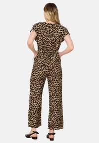 Mono de leopardo de tela elástica con mangas cortas, cintura entallada y piernas anchas. Llevado con sandalias de tacón negras con lazos.