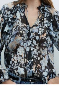 Sheer black floral blouse with ruffled neckline, buttons down the front, and long sleeves. Features blue, peach, and white floral patterns.