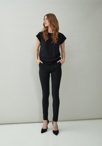 Zwart kortemouwen top gecombineerd met zwarte slim-fit broek en zwarte puntige hakken. De stof heeft een gladde textuur met minimale details.