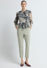 Peplum blouse in grijs en beige met bloemmotief, gecombineerd met lichtgroene, op maat gemaakte broek en bordeauxrode hakken. Zachte stof, nauwsluitend ontwerp.