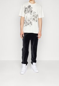 Camiseta de manga corta blanca con gráficos negros intrincados; combinada con pantalones joggers de terciopelo negro y zapatillas blancas.
