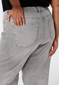Pantalon en denim gris avec une coupe décontractée, doté de poches arrière et d'une texture lisse. La taille comprend des passants de ceinture pour plus de fonctionnalité.