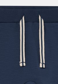 Mørkeblå shorts med teksturert stoff, elastisk midjebånd med hvite snorer og sidespalter for justerbar passform.