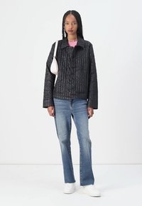 Svart vadderad jacka med knappstängning, stora fickor och avslappnad passform. Matchad med blå jeans och vita sneakers. Minimalistisk rosa handväska.