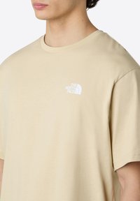 Beige tričko vyrobené z měkké bavlny, s kulatým výstřihem a krátkými rukávy. Malé bílé logo na levé části hrudi.