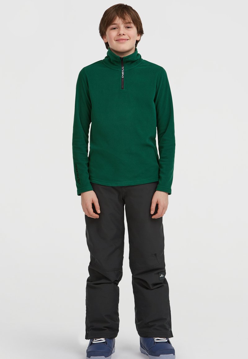 Pullover in pile verde con colletto alto e zip a quarti, abbinato a pantaloni da neve neri e stivali blu, su sfondo bianco.