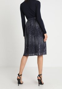 Jupe en sequins bleu marine avec une silhouette évasée, comportant des rayures verticales et une taille élastique. Associée à des sandales à talons hauts noires à lanières.