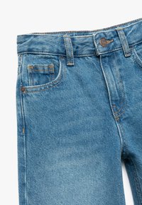 Jeans de denim azul con un acabado desgastado, que cuentan con cinco bolsillos, costuras en color naranja y un cierre de botón en la cintura.