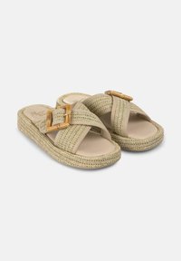 Sandali beige intrecciati senza chiusura con un design testurizzato, caratterizzati da due cinturini incrociati e un grande accento in metallo dorato sul lato.