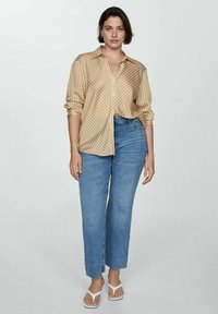 Camicia a righe in morbido tessuto, con bottoni, maniche lunghe e vestibilità rilassata. Un paio di jeans blu a vita alta e sandali bianchi.