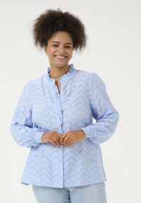 Chemise bleu clair à boutons avec un col froncé et de longues manches bouffantes. Présente un motif en chevrons et des poignets élastiques.