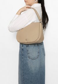 Sac à dos en cuir beige avec une forme structurée, un rabat supérieur, des détails de couture et un accent en métal argenté.