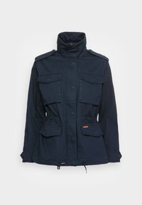 Granatowa kurtka z wysokim kołnierzem, czterema kieszeniami z przodu, regulowanym pasem i ściągaczem u dołu; wykonana z trwałej bawełnianej tkaniny.