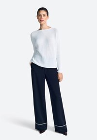 Biely pletený sveter s okrúhlym výstrihom v páre s čiernymi vysokými nohavicami s bielym lemom na leme. Hladká textúra.