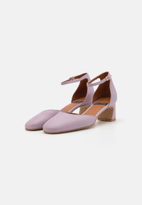 Chaussures à talon bloc en cuir lilas avec un bout pointu et une sangle à la cheville, ornées d'une boucle en ton doré. Texture lisse et design minimal.