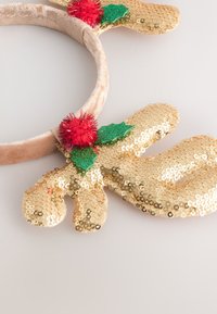 Gold sequined reindeer ear headband with plush beige base, red pom-poms, and green holly accents.