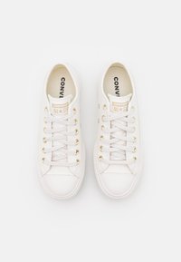 White canvas sneakers with gold eyelets, round toe, and textured rubber sole. Branding printed on the insole. Laces for secure fit.