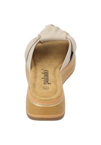 Beige Slippers mit einem geknoteten Oberteil, weichem, wildlederähnlichem Innenfutter, dicker, tansfarbener Außensohle und einer hellen Akzentlinie an der Basis.
