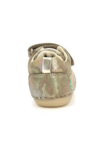 Zapato infantil beige con acentos metálicos multicolores, forro interior suave, tira de velcro y una suela baja y flexible.