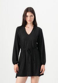 Čierne šaty z broderie anglaise látky, s výstrihom do V, dlhými rukávmi, elastickými manžetami a detailom viazaného pásu.