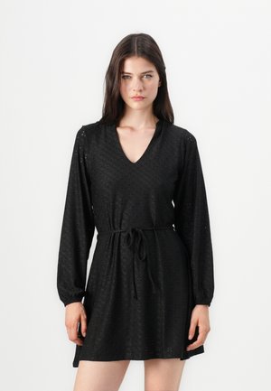 Robe noire en tissu broderie anglaise, avec un décolleté en V, des manches longues, des poignets élastiques et un lien à la taille.
