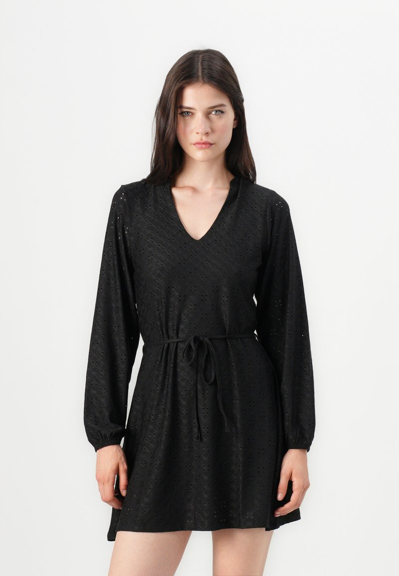 Čierne šaty z broderie anglaise látky, s výstrihom do V, dlhými rukávmi, elastickými manžetami a detailom viazaného pásu.