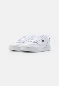 White athletic sneakers made of synthetic material, featuring a low-top design, round toe, and textured rubber sole, with black logo detail.