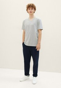 Camiseta de algodón gris con cuello en V combinada con pantalones azul marino y zapatillas blancas; corte relajado con mangas cortas y diseño minimalista.