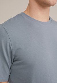 Camiseta de algodón gris con cuello redondo, mangas cortas y textura suave, mostrando un primer plano del área del torso superior.