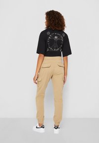 Svart kortärmad t-shirt med grafisk design på baksidan, kombinerad med beige cargo-byxor med sidfickor, och vita sneakers med svarta accenter.