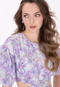 Blomster crop top i pastelfarver med puffærmer, rund halsudskæring og udskårne detaljer. Stoffet har et let, tekstureret udseende.