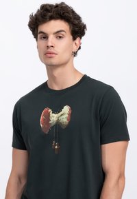 Zwarte korte mouwen t-shirt met een afbeelding van een rode en witte gebroken strik met hangende accenten, gemaakt van katoen.