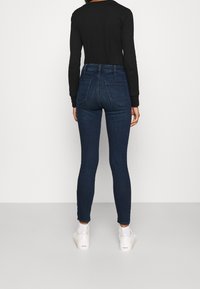 Mörkblå tajta jeans med hög midja, med en mjuk denimstruktur och bakfickor. Matchade med vita sneakers.