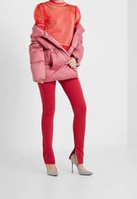 Růžová péřová bunda, průhledný červený top s třpytem, červené legíny a stříbrné lodičky na vysokém podpatku se bočními štěrbinami. Texturované a hladké materiály.