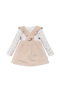 Vestido de pana beige con tirantes de volantes sobre una blusa blanca de manga larga que presenta patrones coloridos de estrellas y arcoíris.