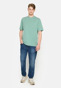 Cămașă verde deschis din bumbac, cu mâneci scurte, asortată cu blugi denimu albastri și adidași crem cu accente gri.