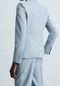 Jasnoniebieski dopasowany garnitur z dobrze skrojoną marynarką z klapami w szpic i akcentami w postaci trzech guzików na mankietach, połączony z pasującymi spodniami.