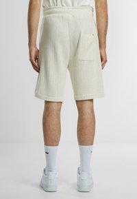 Hvite, ripede strikkede shorts med elastisk linning, med en baklomme og oppbrettede sømmer. Brukt med hvite sneakers og sokker.