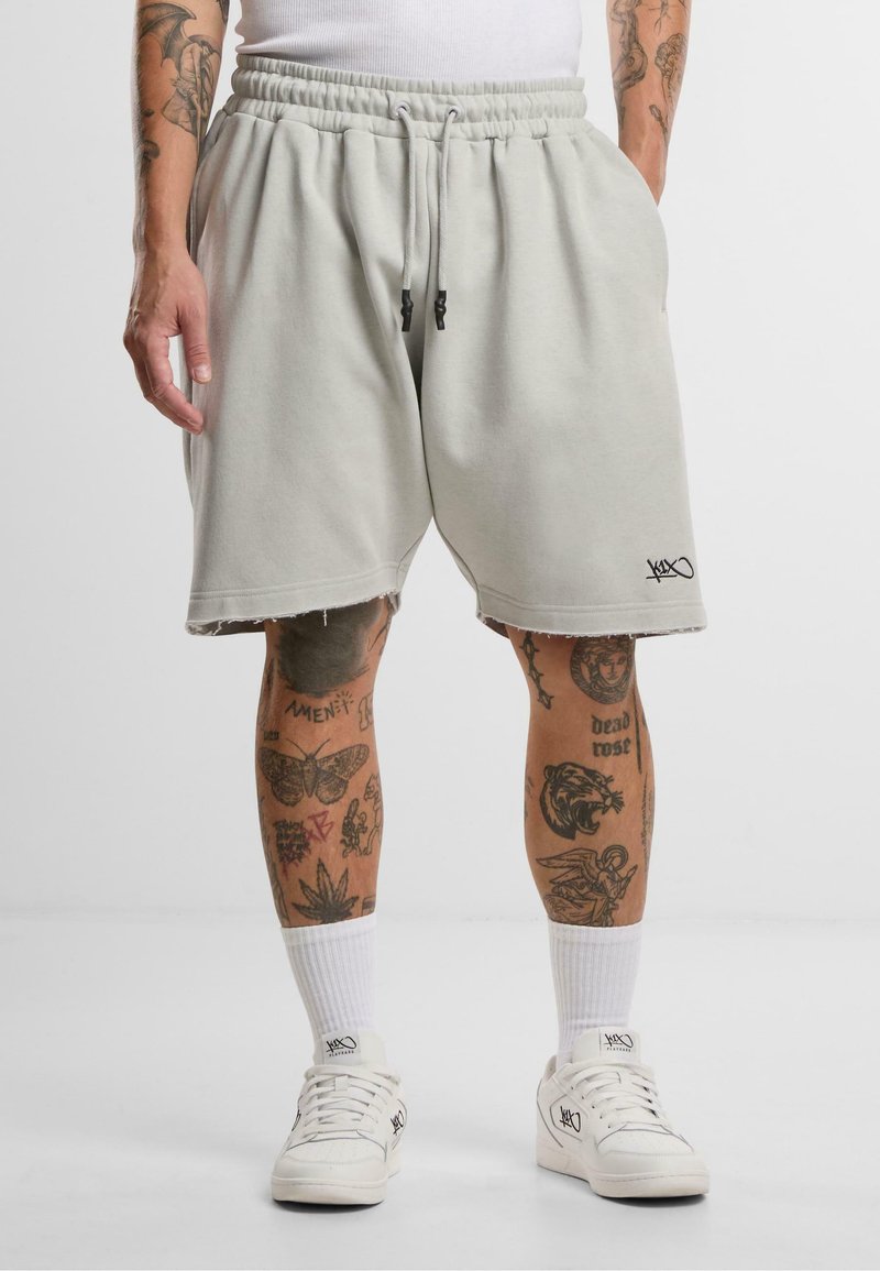 Lys grå, knelengde shorts i mykt stoff med elastisk midjebånd og svarte snorer. Merkbar slitt kant og logo detalj på benet.