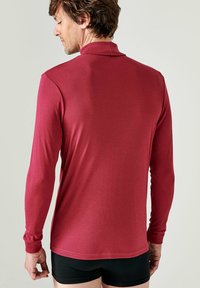 Polo a maniche lunghe rossa con colletto, caratterizzata da una texture liscia e un design aderente, indossata da una persona di spalle.