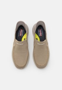 Beige Slipper mit Mesh-Obermaterial, gepolstertem Kragen und strukturiertem Gummisole. Mit Skechers-Logo an der Seite und auf der Innensohle.