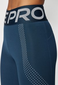 Mørkeblå leggings med en bred elastisk talje med "PRO" bogstaver, glat tekstur og et prikket mønster langs sidesømmen.