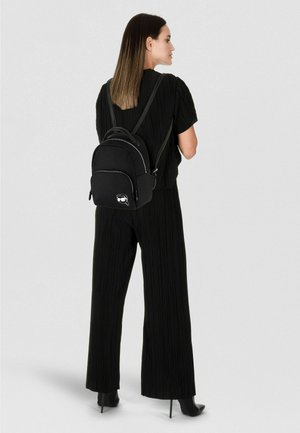 Sac à dos en nylon noir à texture lisse, forme arrondie, double poignée supérieure, fermeture éclair et poche avant avec un logo.