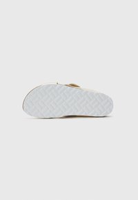Sandal bottom with textured white rubber sole, light beige upper featuring a smooth finish and strap. Patterned tread design for grip.