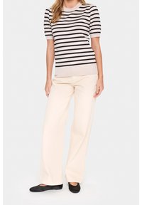 Randig stickad topp i beige och svart, ihop med krämfärgade vida byxor. Modellen har svarta platta skor. En enkel, avslappnad outfit.